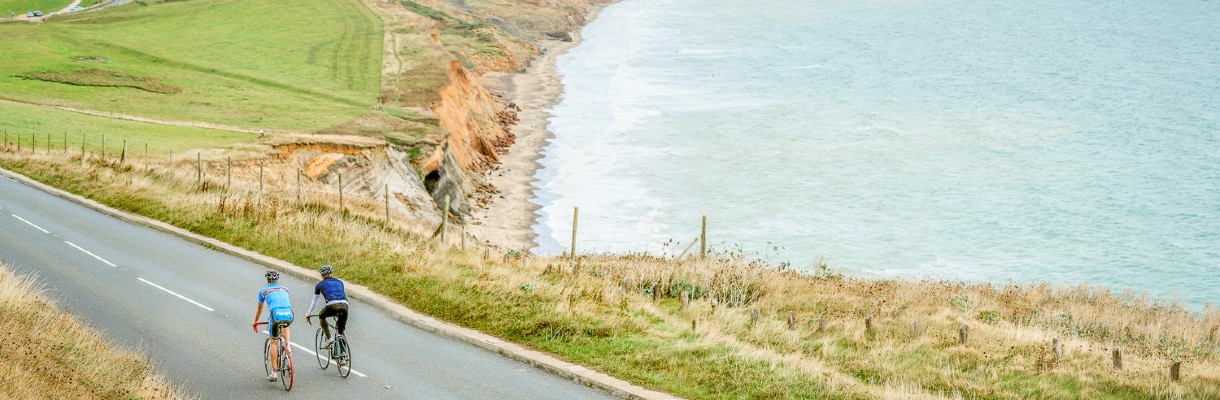 Two men cycling on the road along the coast